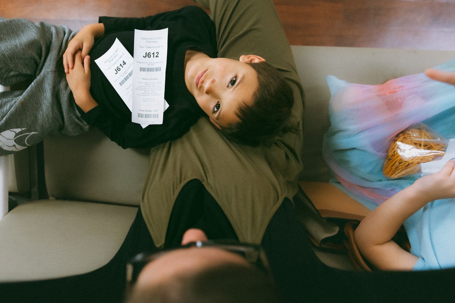 Two people relaxing on a couch, one lying down holding papers, another sitting with a snack.