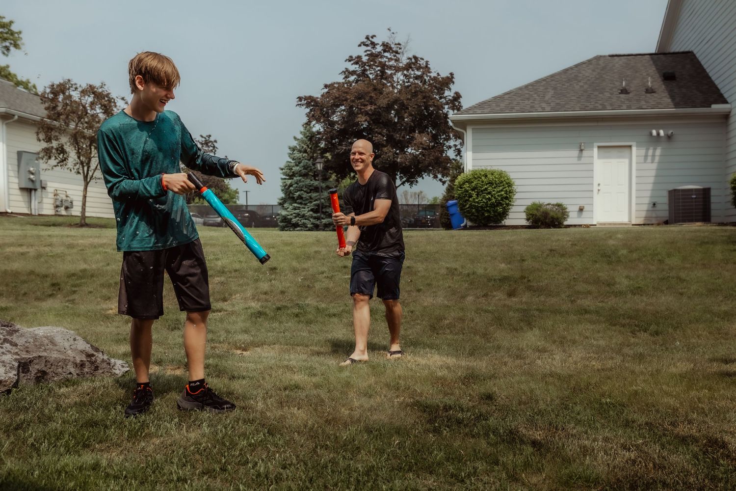 People having fun with water guns in a grassy backyard.