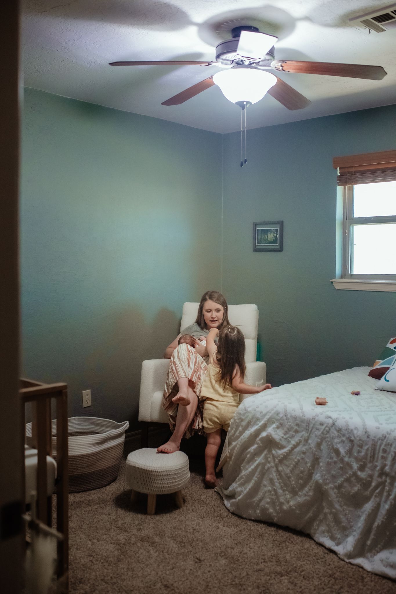 A cozy bedroom interior with sage green walls, white ceiling fan, and natural lighting from a window.