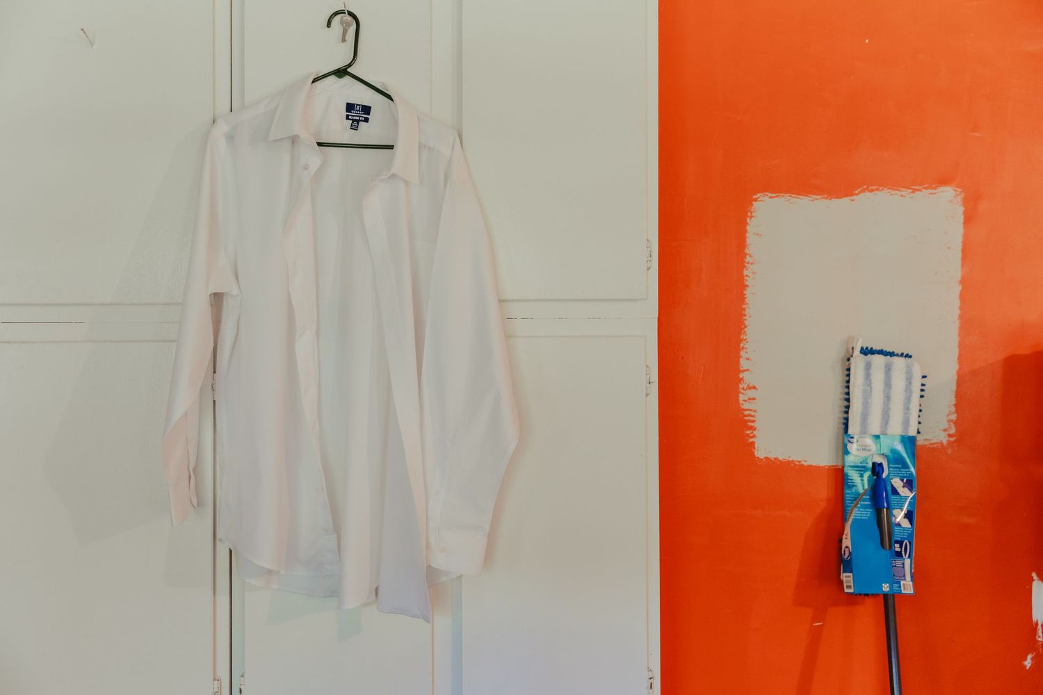 White dress shirt hanging on wardrobe next to orange painted wall with white patch.