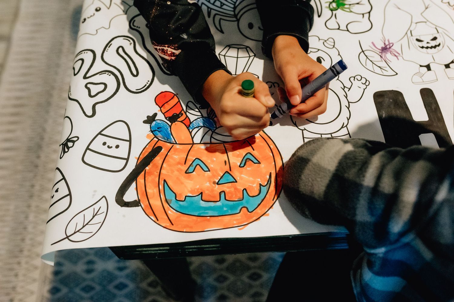 Children coloring a Halloween pumpkin jack-o-lantern drawing with markers on a white coloring sheet.