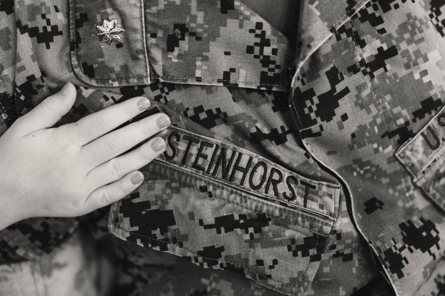 Close-up of a military camouflage uniform with name tape reading Steinhorst, with a hand resting on the jacket.