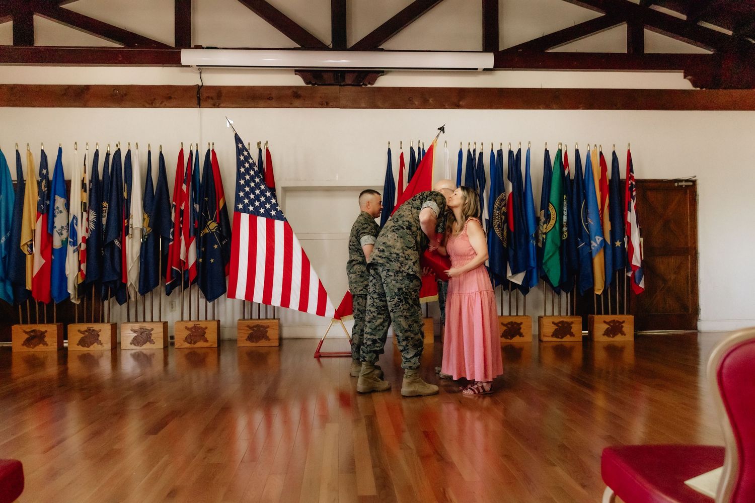 Military soldier embraces family in front of American and state flags during an indoor ceremony.