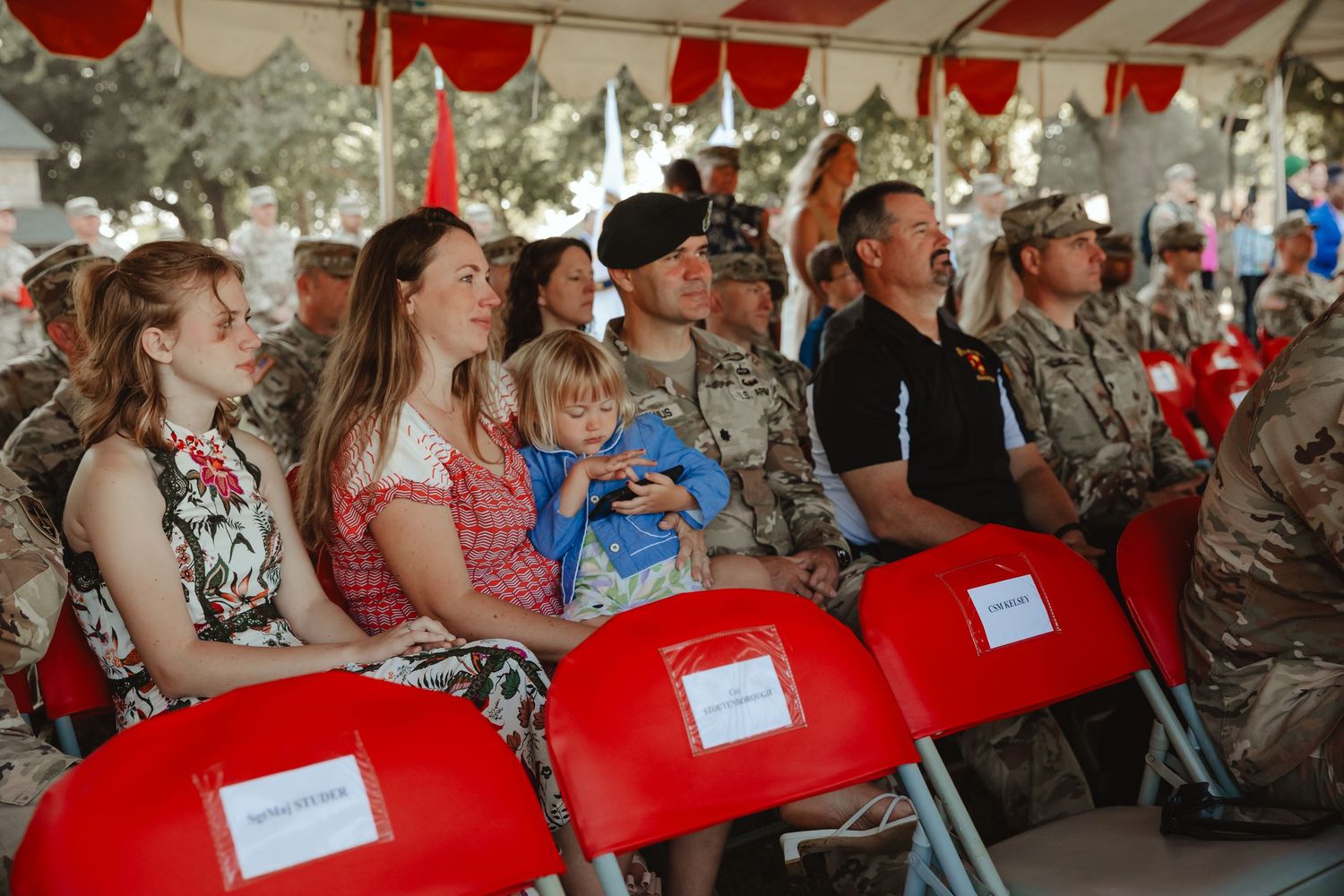 People seated under a red and white striped tent canopy at an outdoor gathering or celebration.
