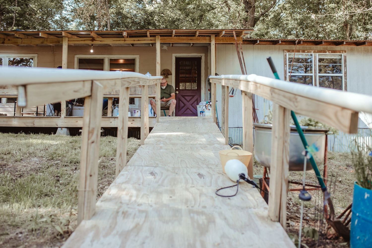 Weathered wooden walkway leading to a rural house with a front porch.