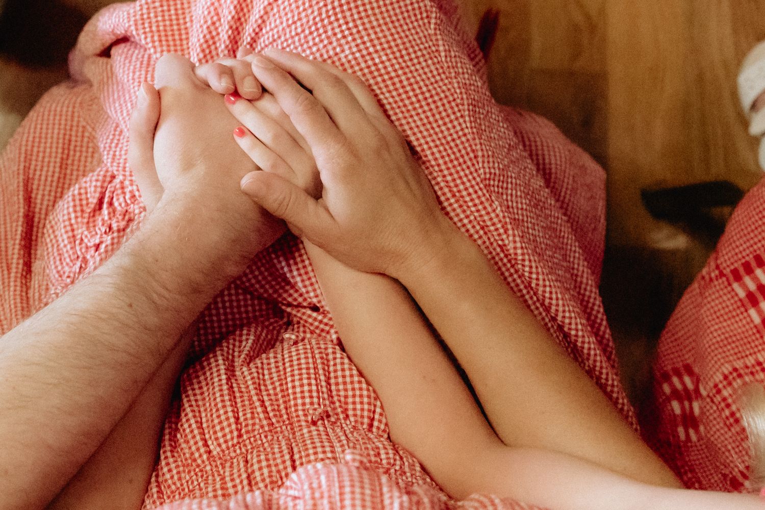 Two people holding hands under a red gingham blanket, sharing an intimate moment together.