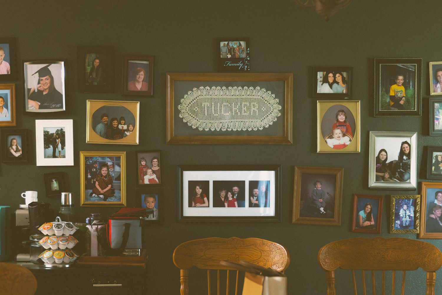 A gallery wall of family photos in various frames on a dark green shows who you are in Mulhall, OK photographer Liz Perez