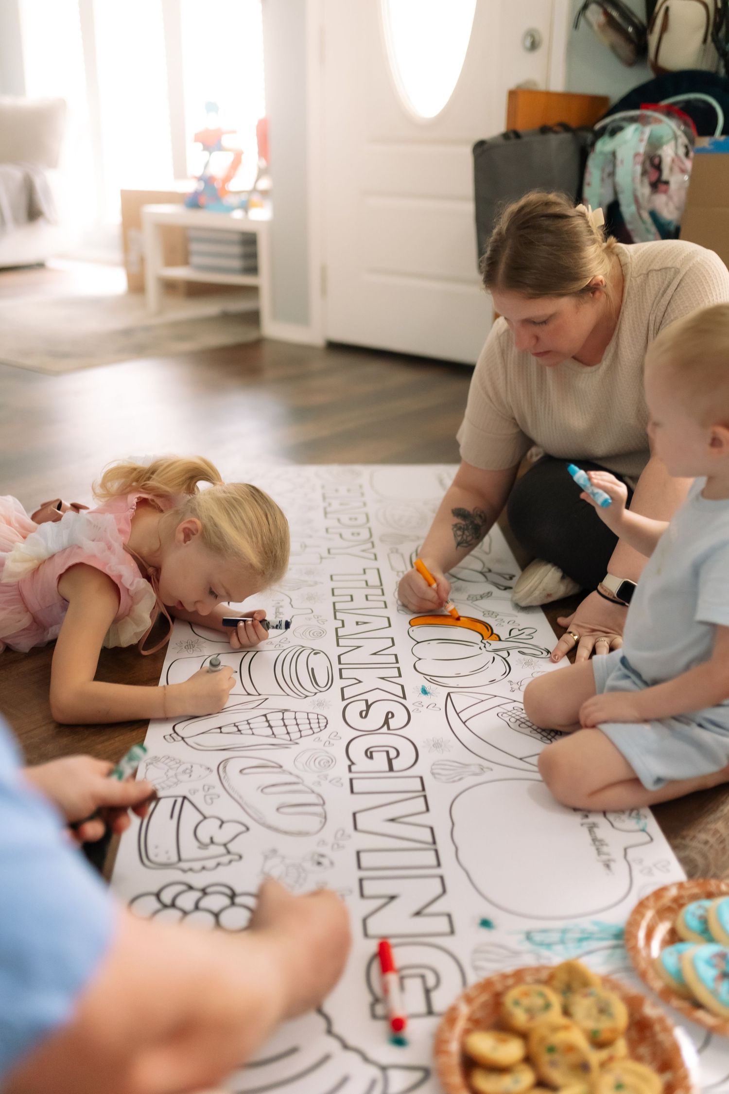 Family coloring a large Thanksgiving themed paper on the floor together with markers and crayons.