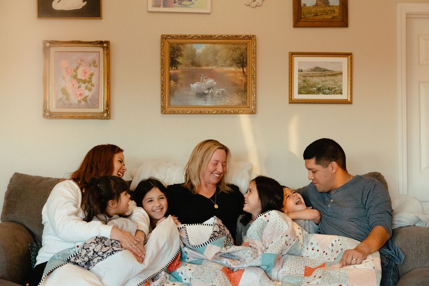 People gathered on a couch in a living room with framed artwork on the walls.