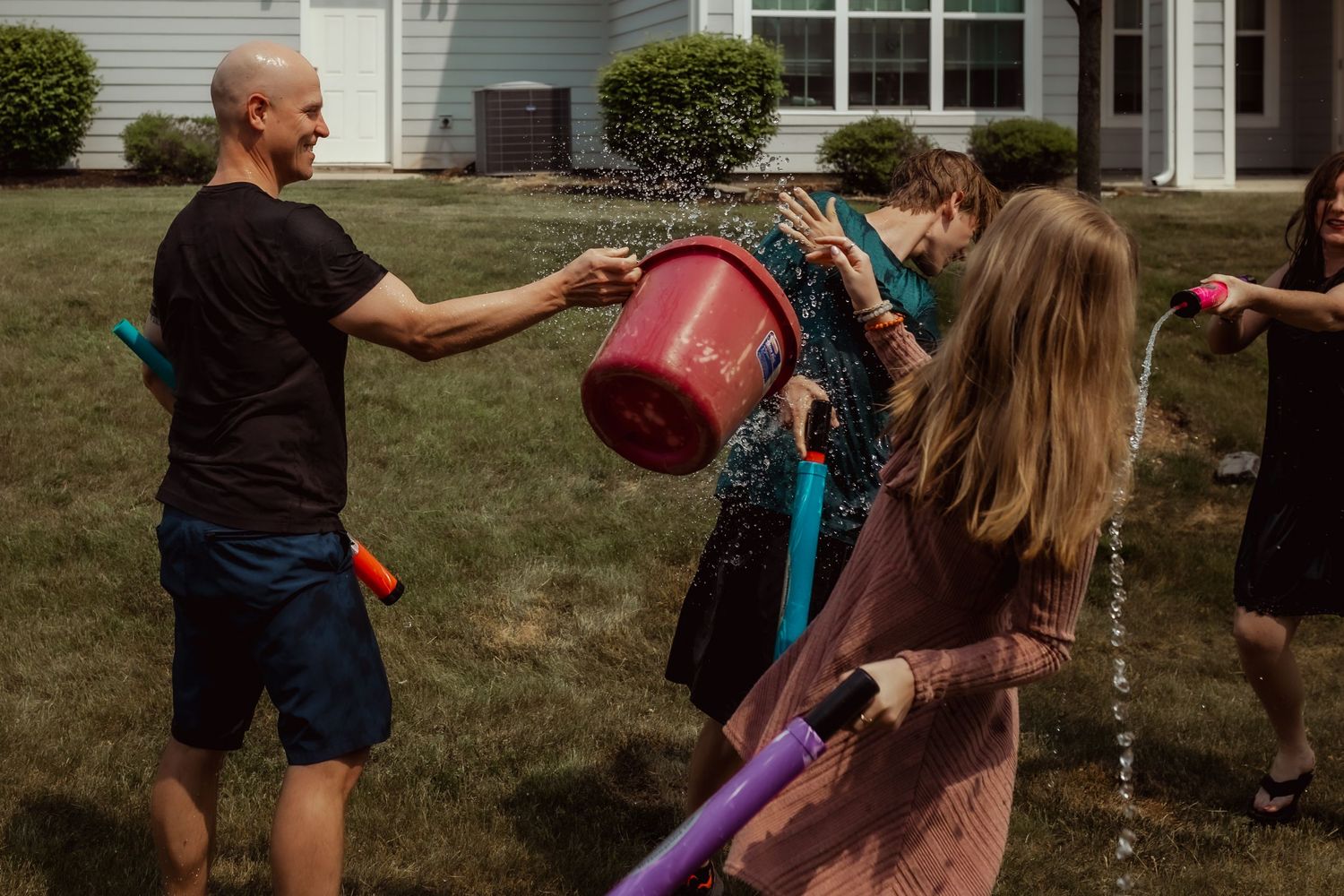 People splashing water and playing with colorful water guns during an outdoor summer activity.