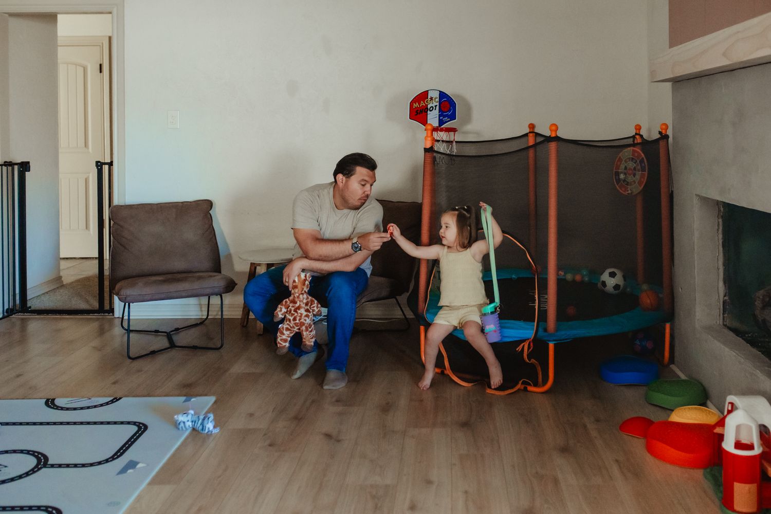 Family enjoying playtime together in living room with mini trampoline and toys on hardwood floor.
