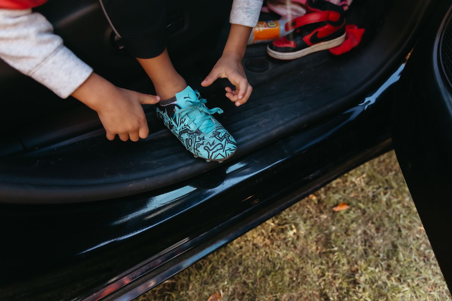 Person wearing bright turquoise running shoes sitting in a black car with red trim.