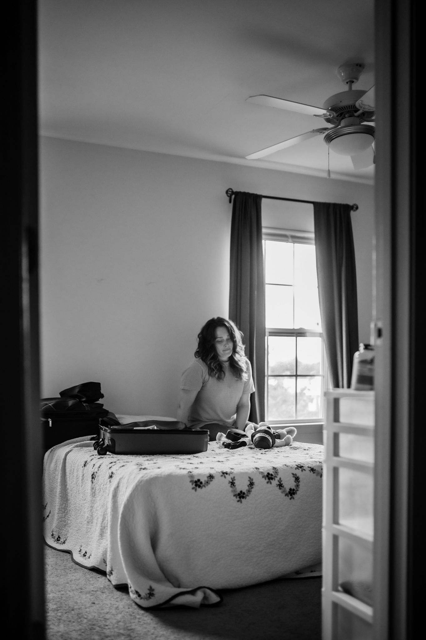 Person sitting on bed with vintage suitcase in black and white photography.