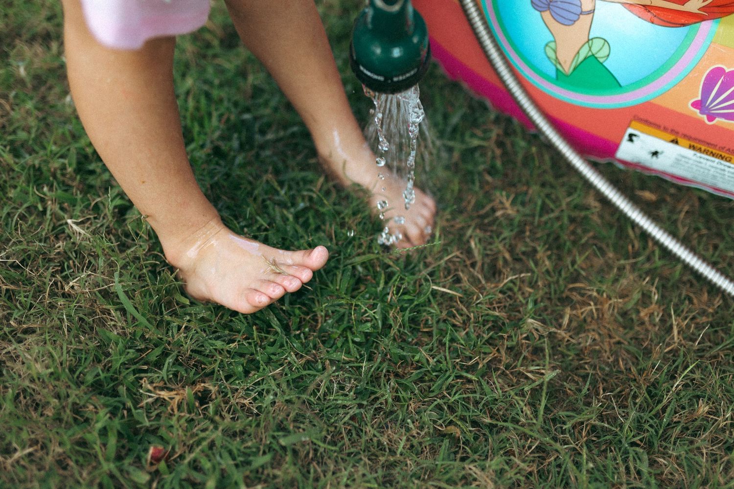 Bare feet standing in grass beside colorful toys spread out during outdoor playtime. In-Home Photography Liz Perez