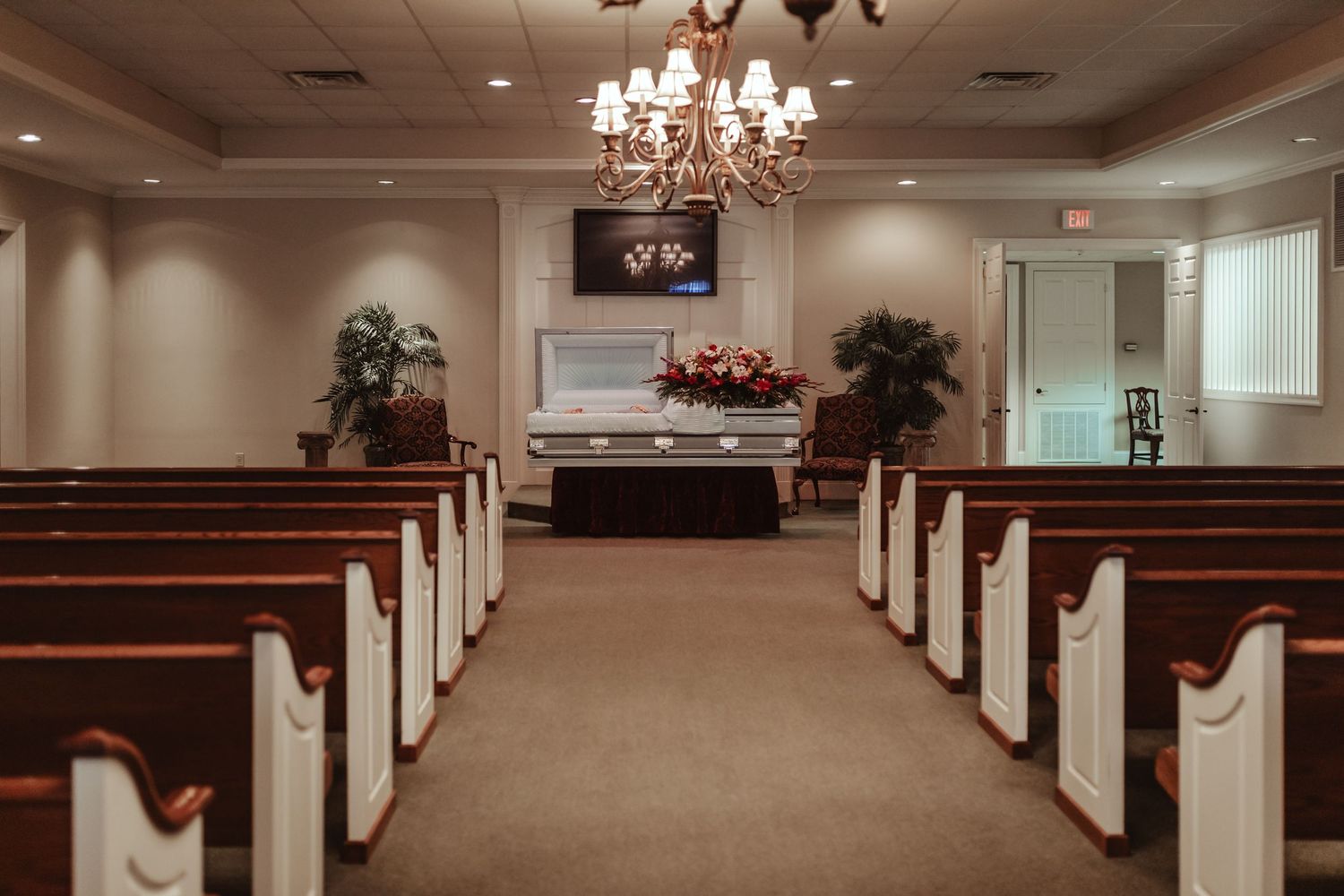 Interior of a funeral home chapel with empty wooden pews and an elegant chandelier hanging from the ceiling.