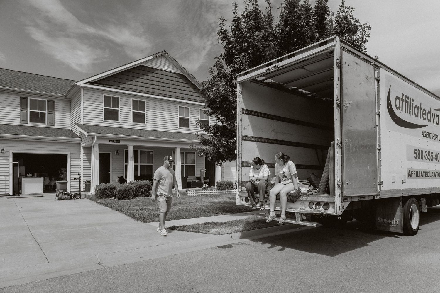 Moving truck parked outside a suburban home with movers loading furniture on a sunny day.