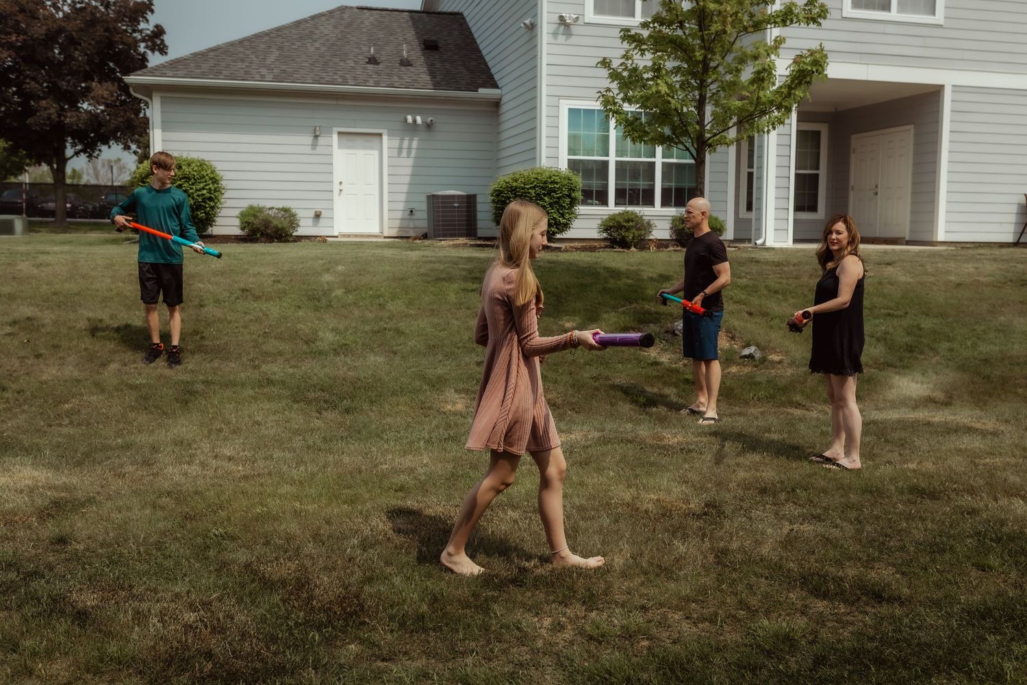 People having fun with water guns on a sunny lawn in front of a house.