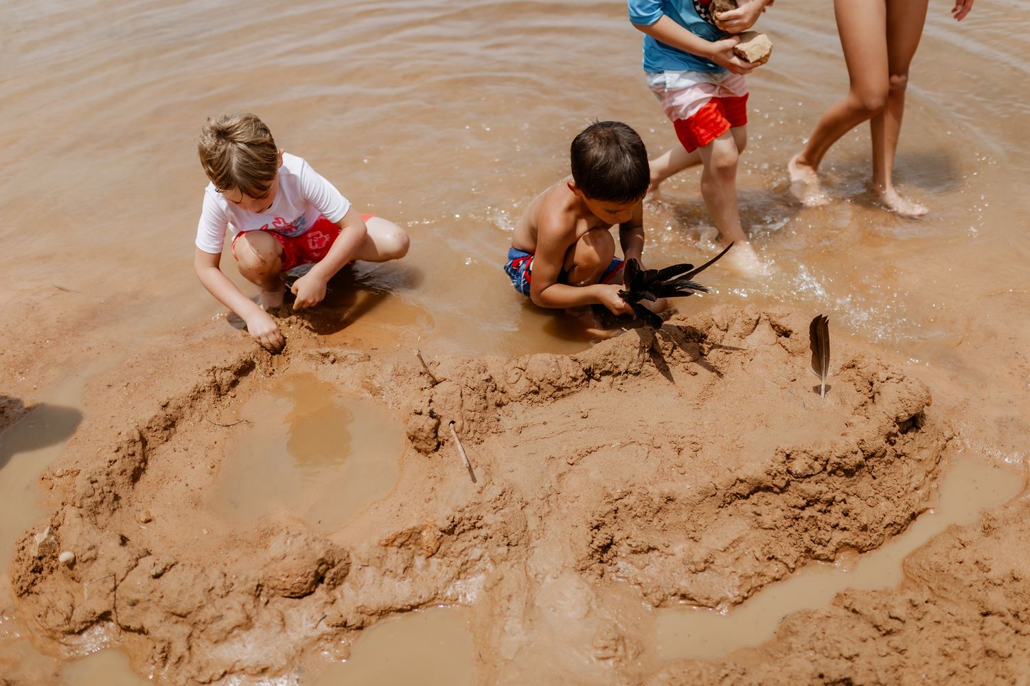 Children playing together in muddy water creating sand structures on the shore.