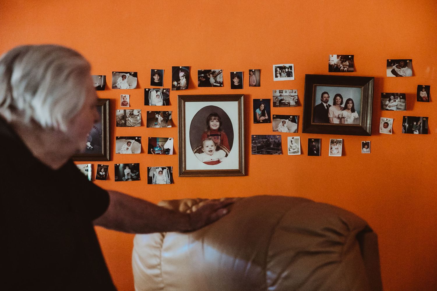 Person looking at collection of framed photographs displayed on bright orange wall.