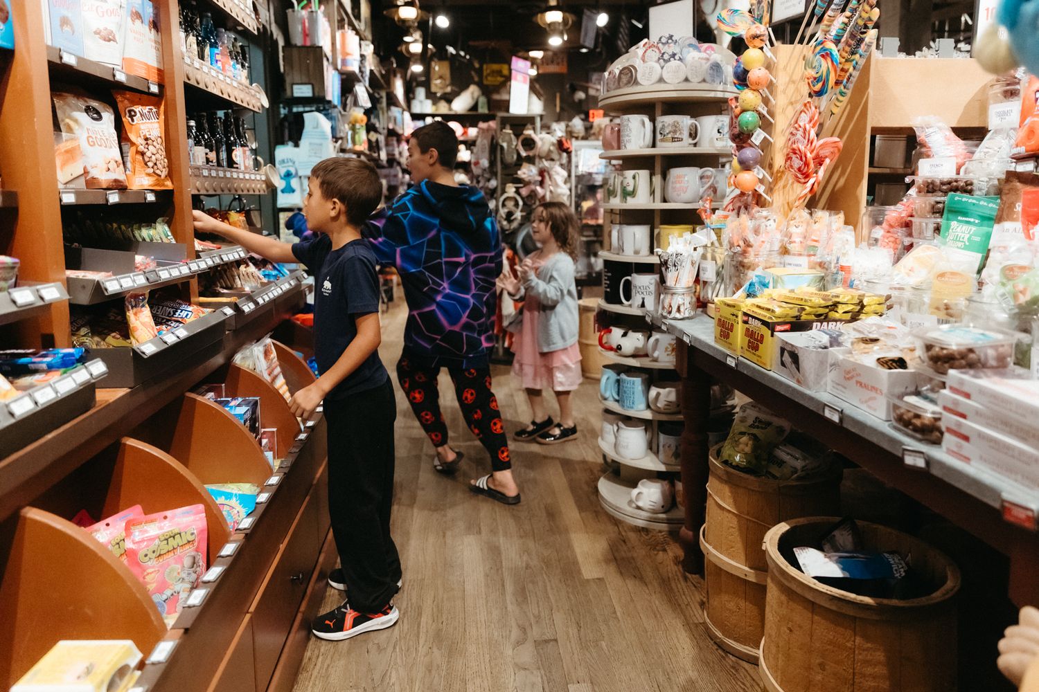 Customers browse merchandise inside a retail shop with wooden floors and well-lit display shelves.