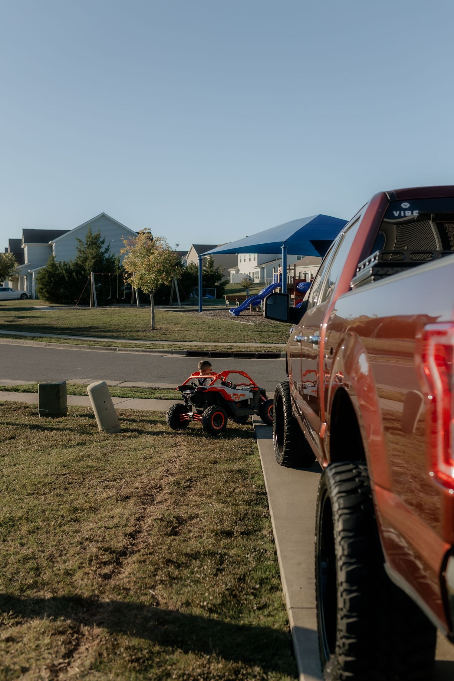 Red pickup truck parked near playground equipment on a sunny day.