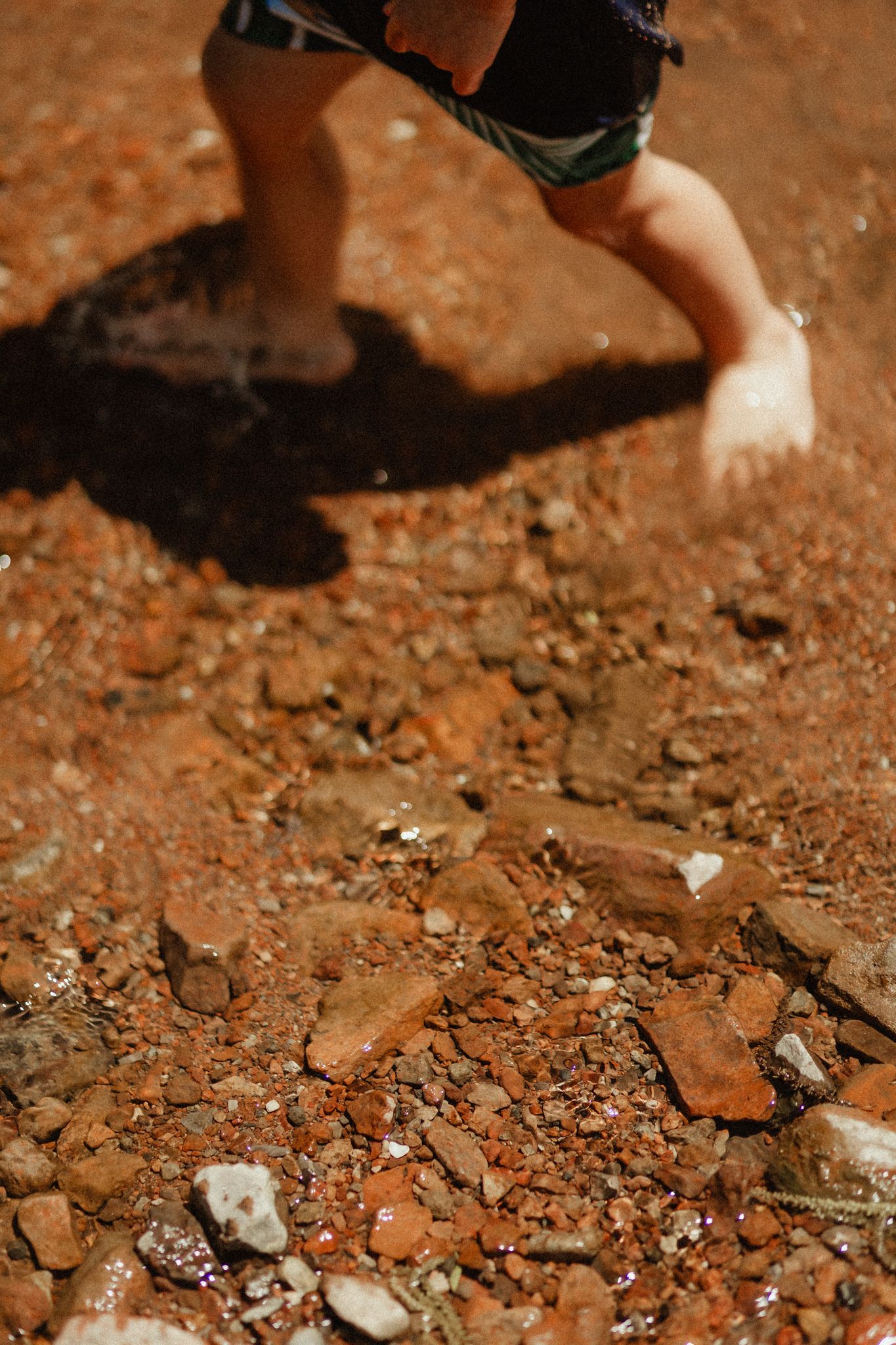 Bare feet walking on rocky red soil with dramatic shadows.