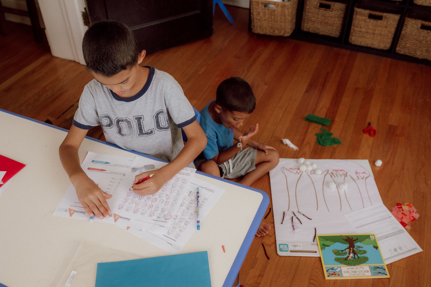 Two people drawing and creating artwork together at a low table with art supplies.