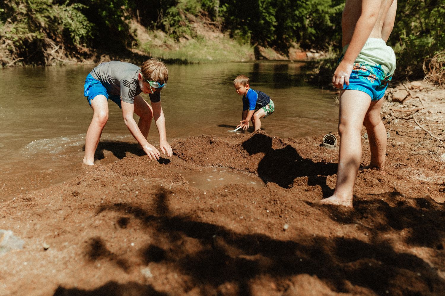 Kids digging and playing in the mud by a river's edge.