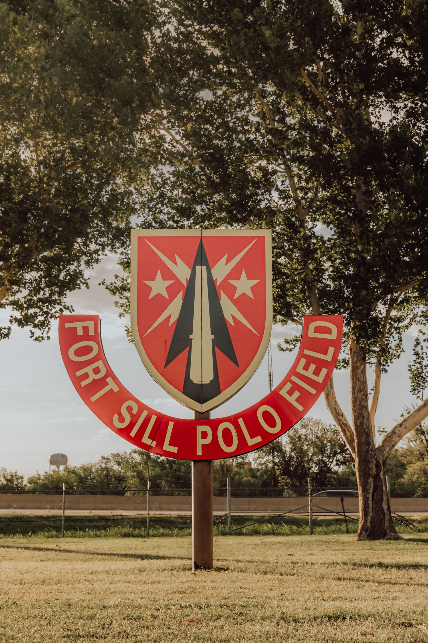 A series of red military insignia signs with arrows displayed across a grassy field with trees in the background.