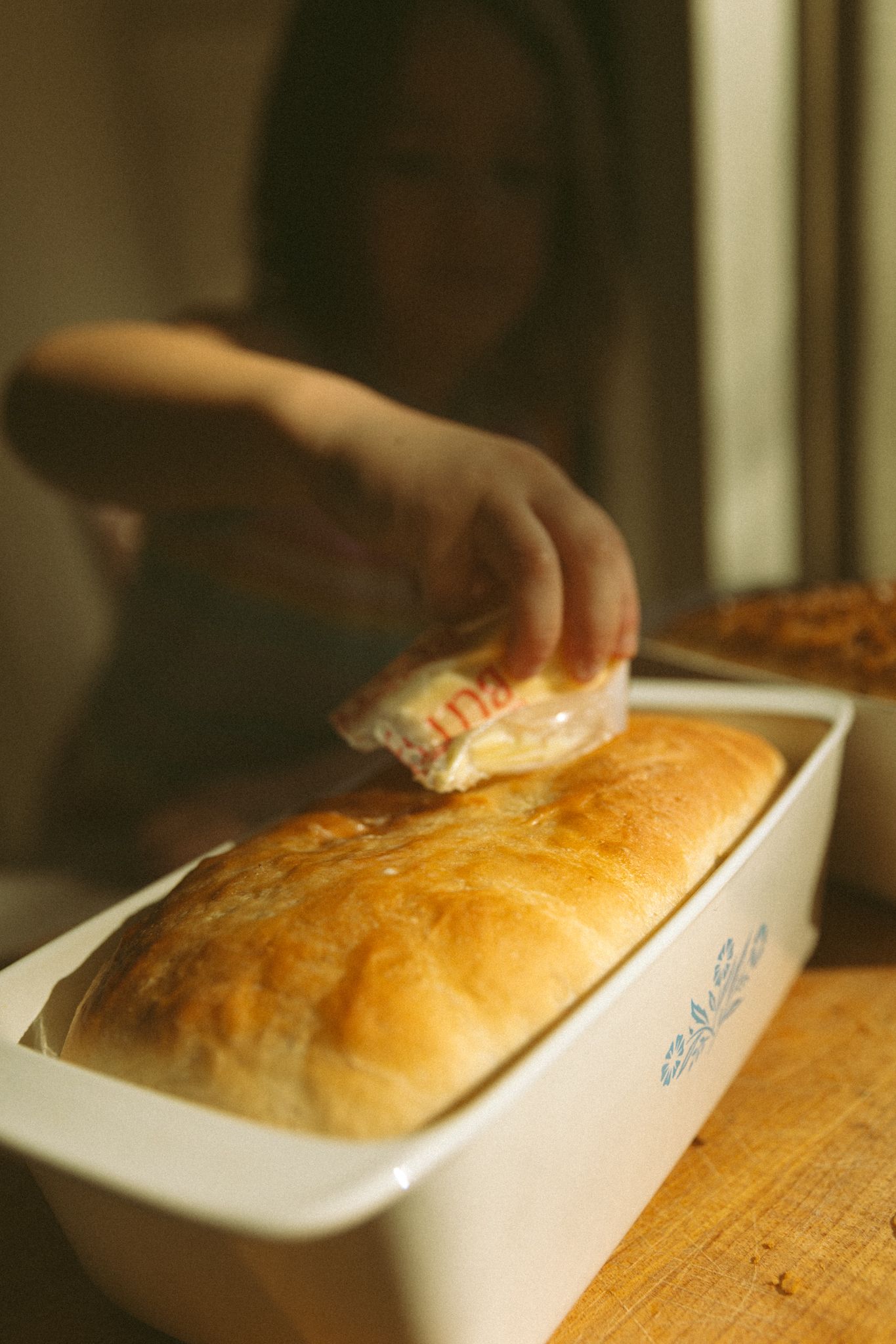 Hands preparing bread dough in white baking dishes on a wooden surface.