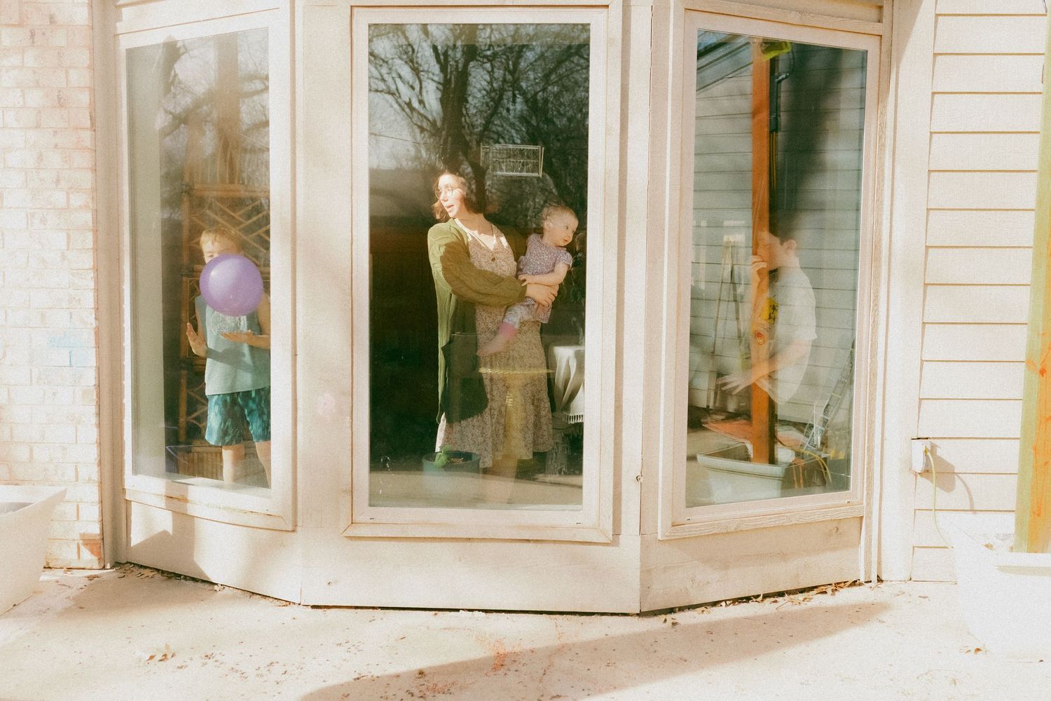 A series of bay windows with white trim on a house exterior creates an elegant architectural feature show casing a mother and her children.