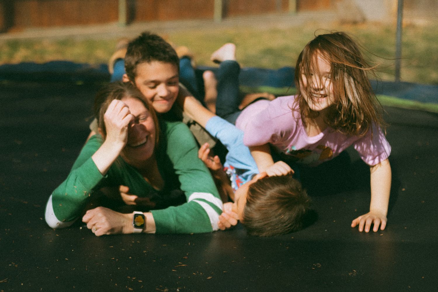 Kids laughing and playing together on a trampoline outdoors on a sunny day.