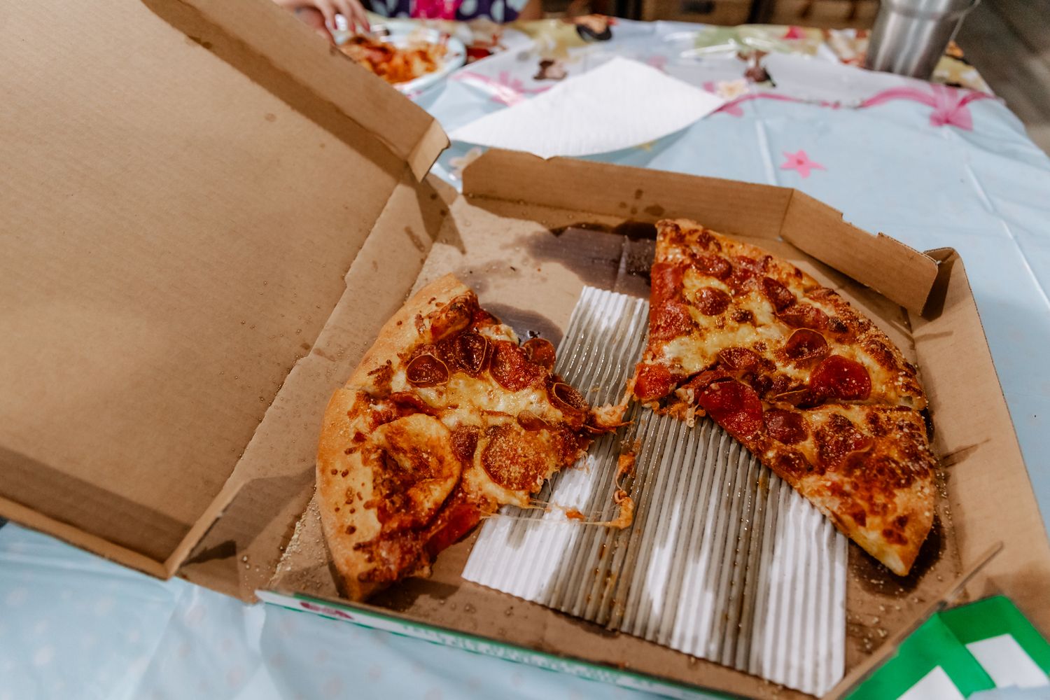A partially eaten pepperoni pizza sits in an open cardboard delivery box on a table with scattered papers.