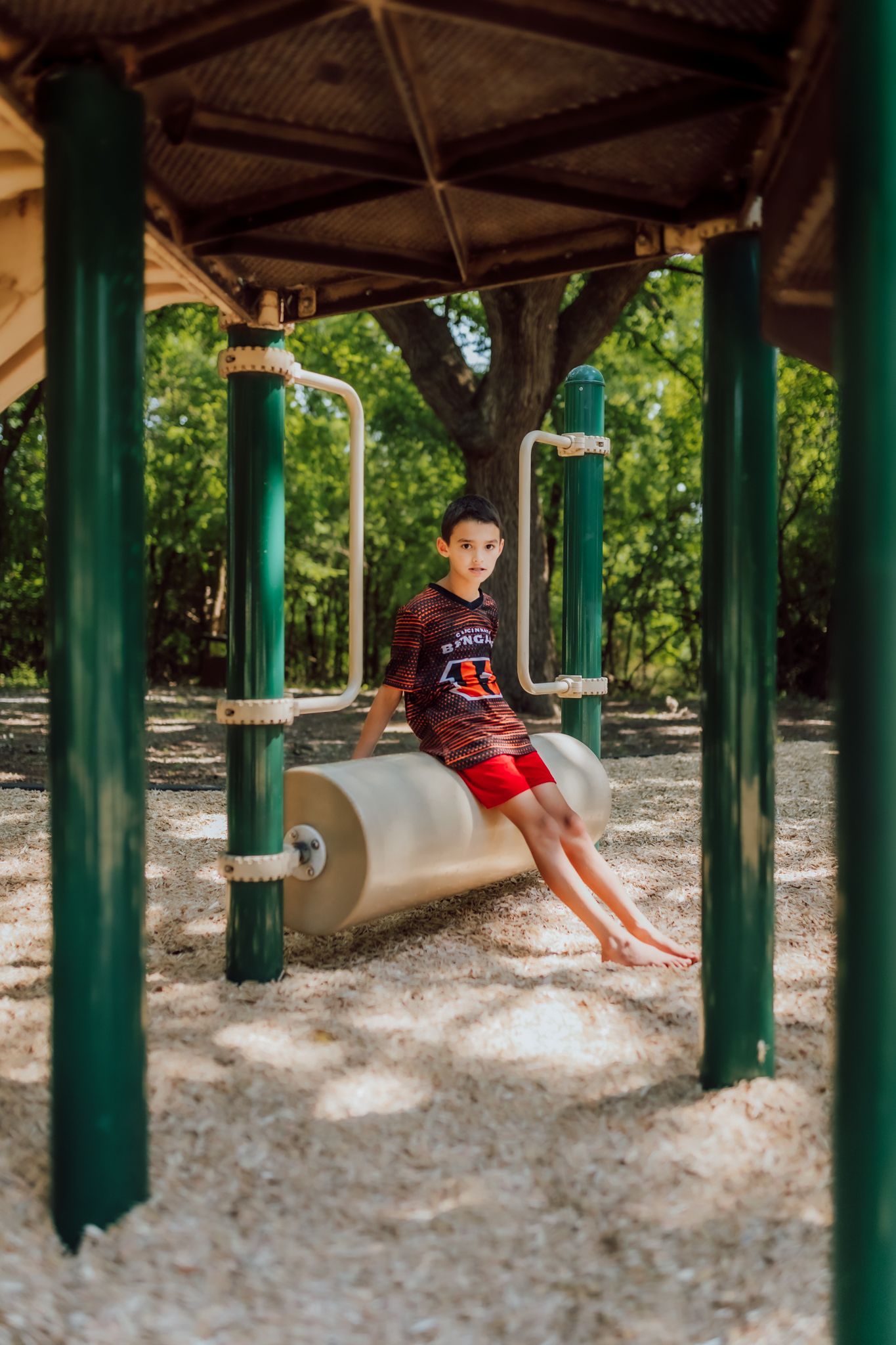 A covered playground area with a roughhousing surface underneath green support columns.