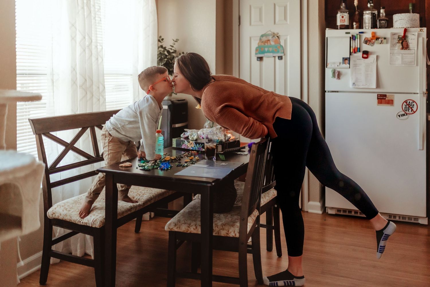 Intimate moment between two people in a kitchen with a dining table and refrigerator.