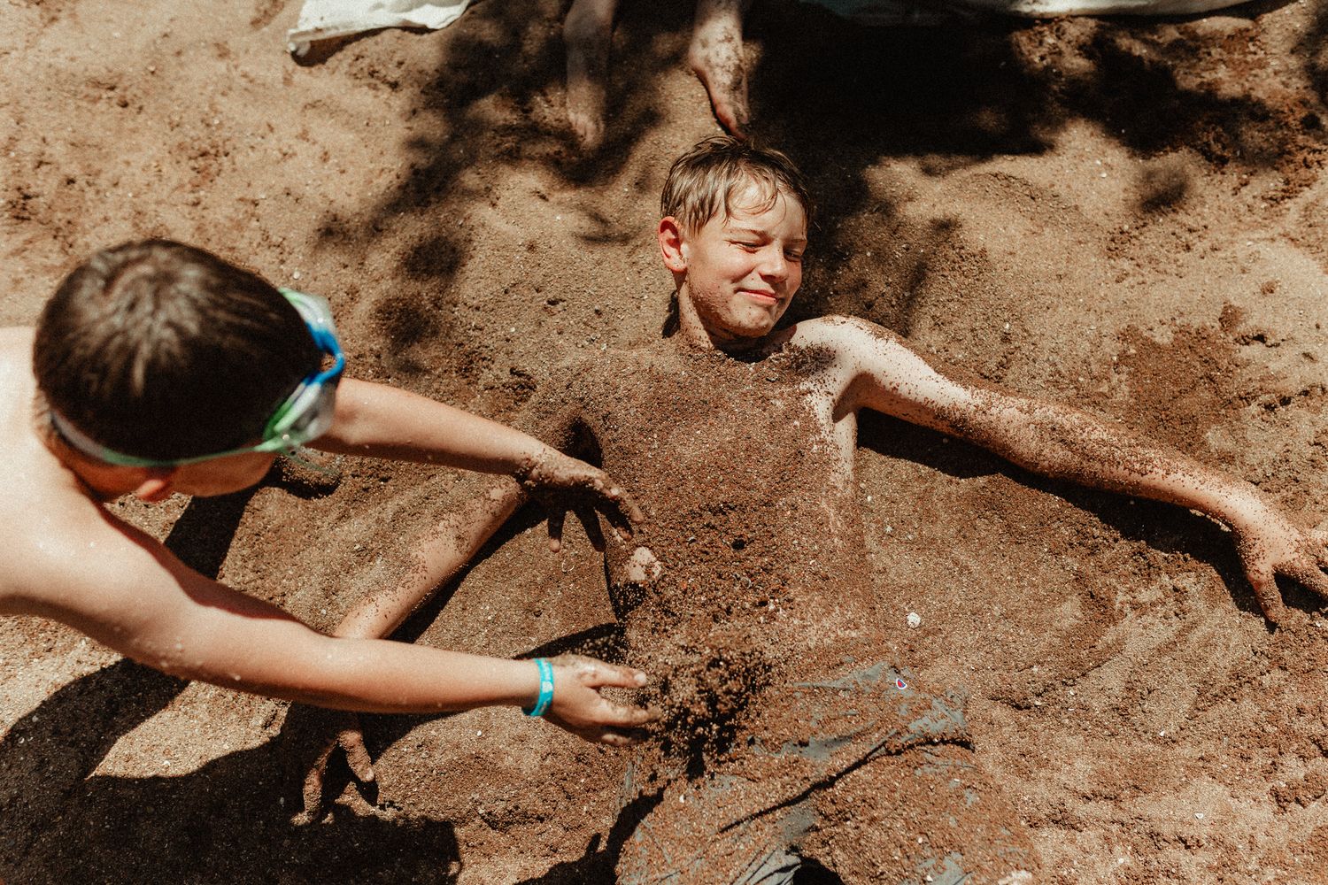 Children playing and getting muddy in dirt on a sunny day.