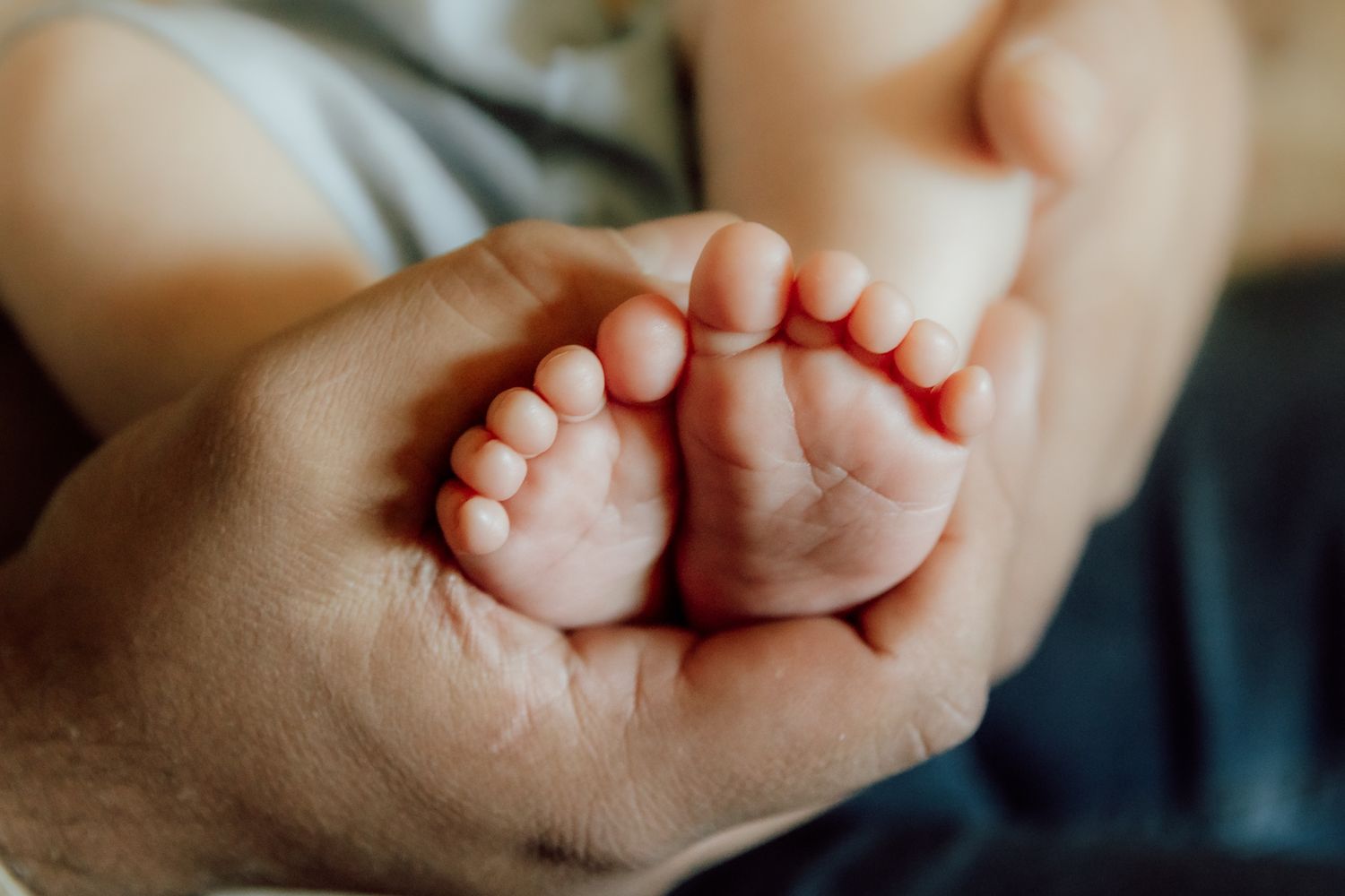 Tiny baby feet being gently held in adult hands against a soft blurred background.