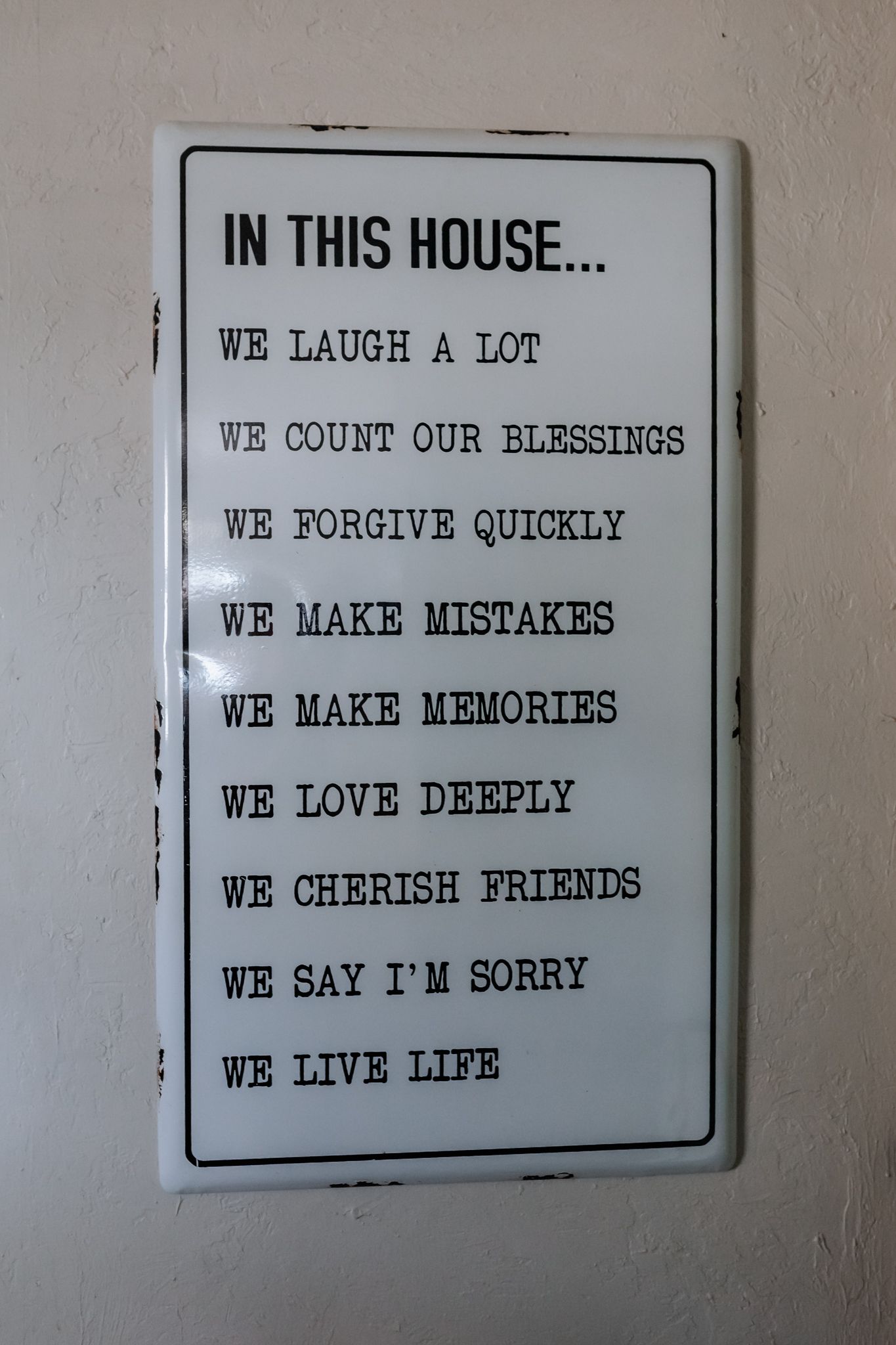 A white sign with house rules listing values like laughter, forgiveness, love and making memories hangs on a wall.
