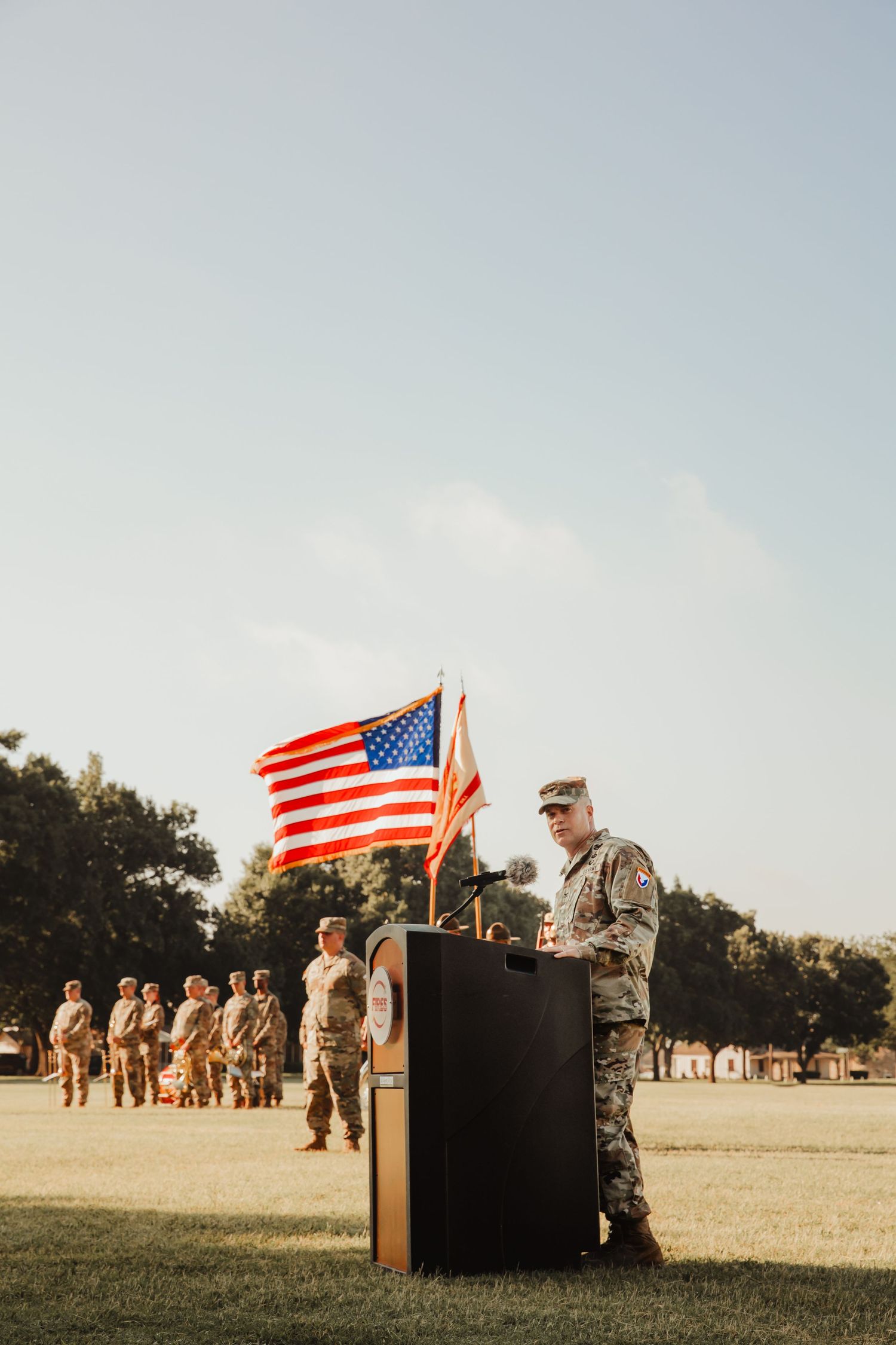 Military ceremony on an open field with American flag and soldiers standing in formation at sunset.