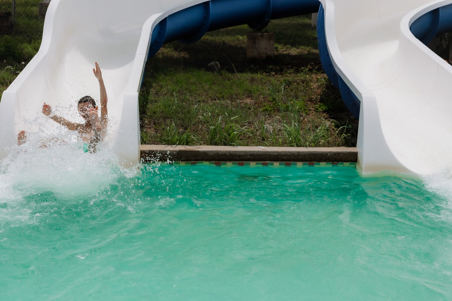 Child making big splash while sliding into turquoise pool water.
