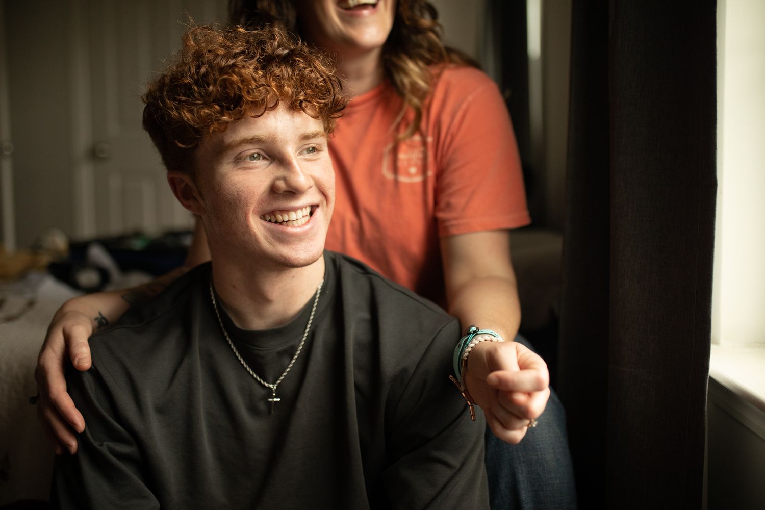 Natural light photo capturing spontaneous laughter and happiness between two people. In-Home Photography Liz Perez