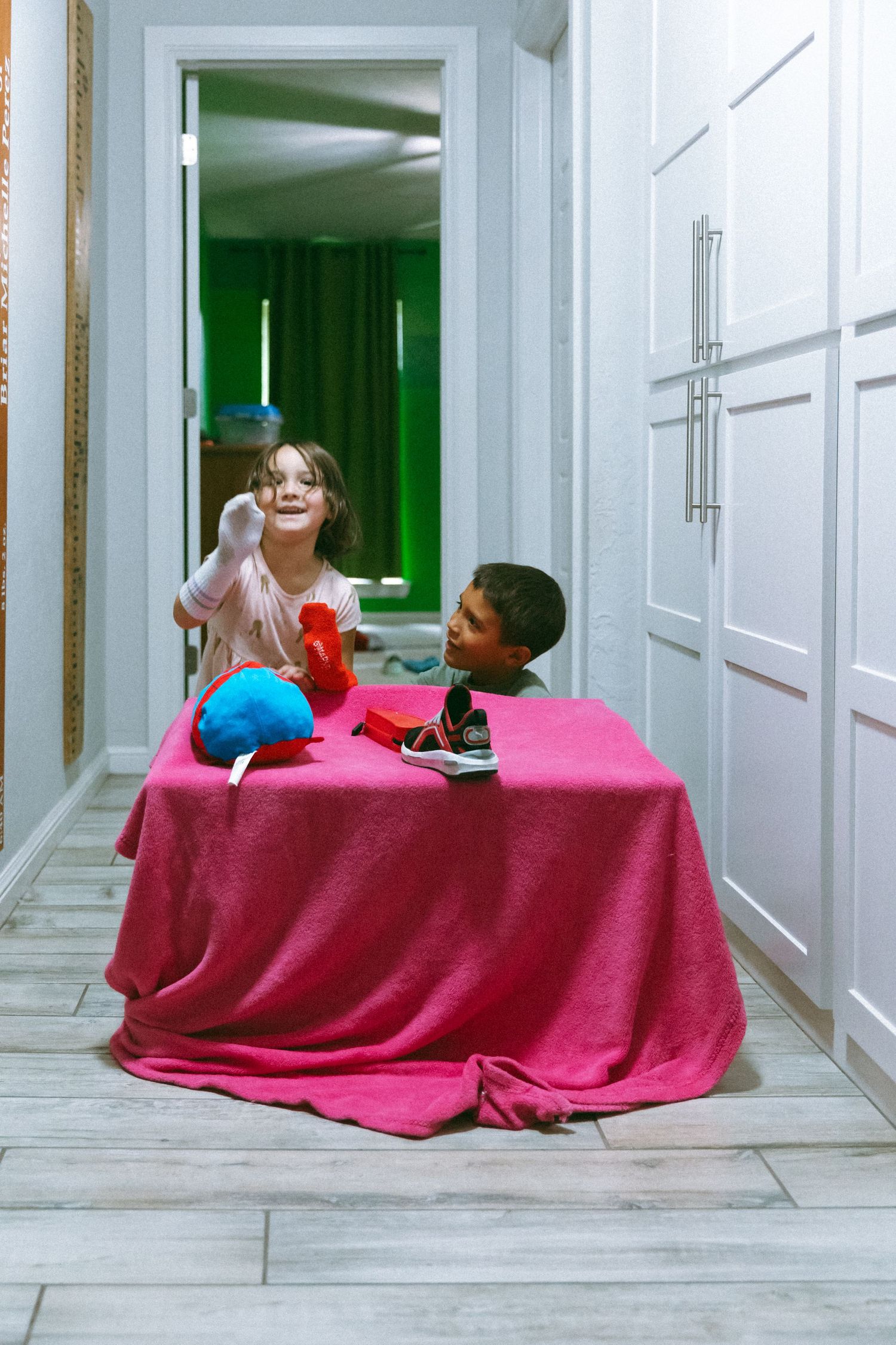 A series of four photographs showing a person under a pink blanket on the floor of a white hallway.