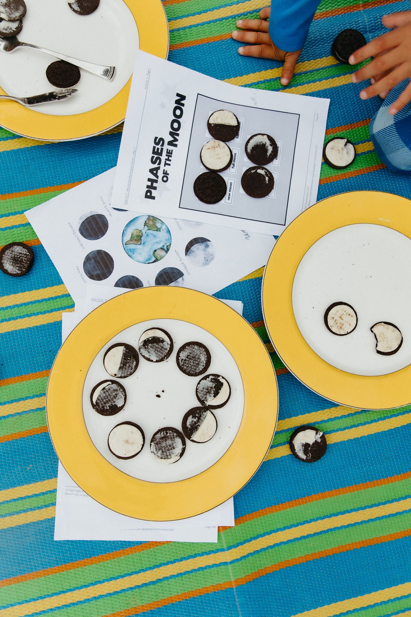 Educational moon phase activity with paper plates and circle diagrams displayed on a colorful striped tablecloth.