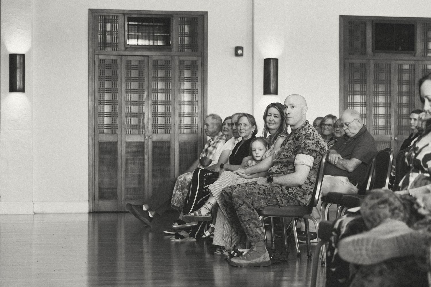 Black and white photo of audience members seated in chairs inside a formal hall during a ceremony or event.
