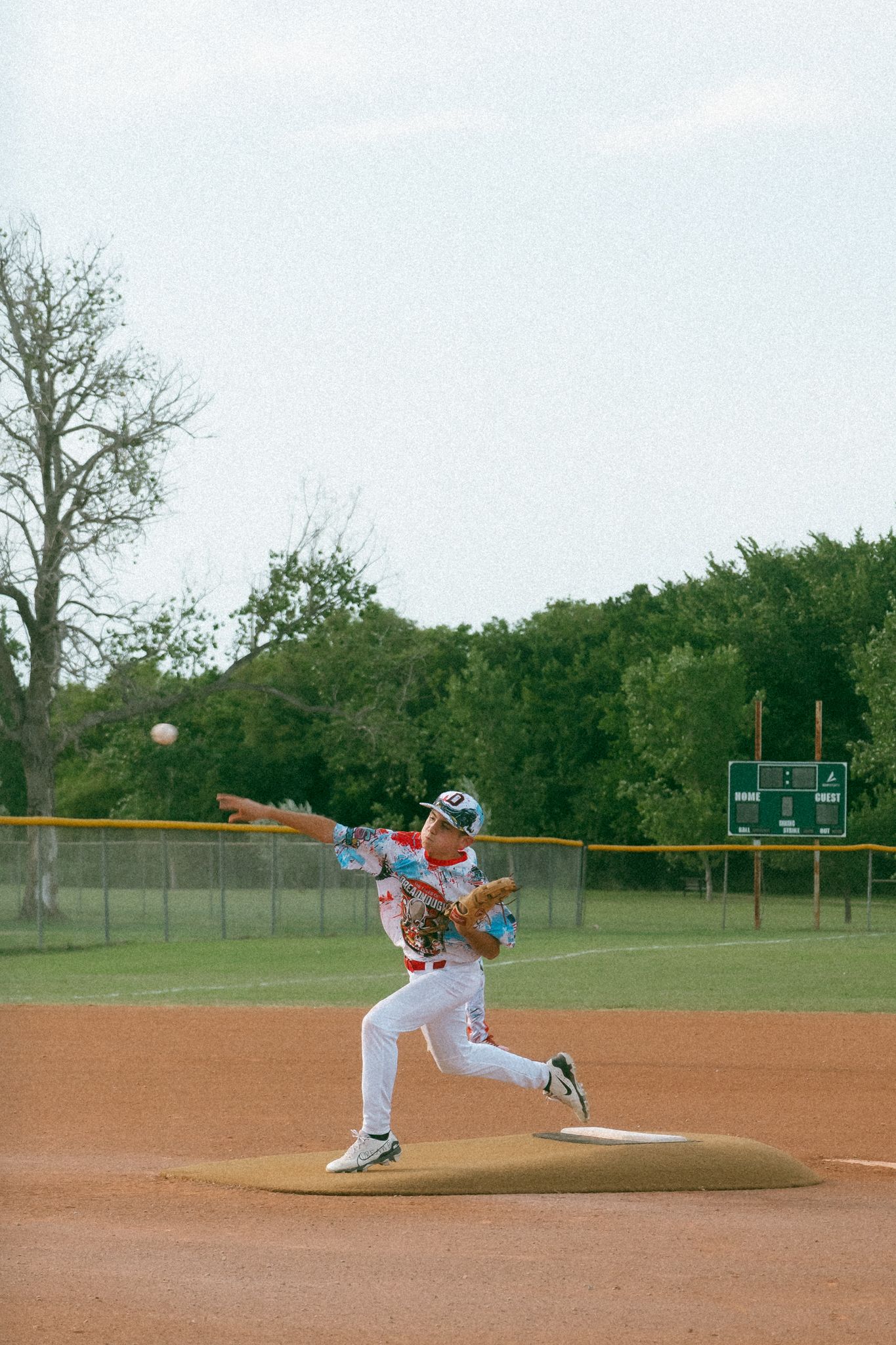 Baseball pitcher in colorful jersey mid-throw on a dirt mound at an outdoor field taken by Documentary photographer Liz Perez.