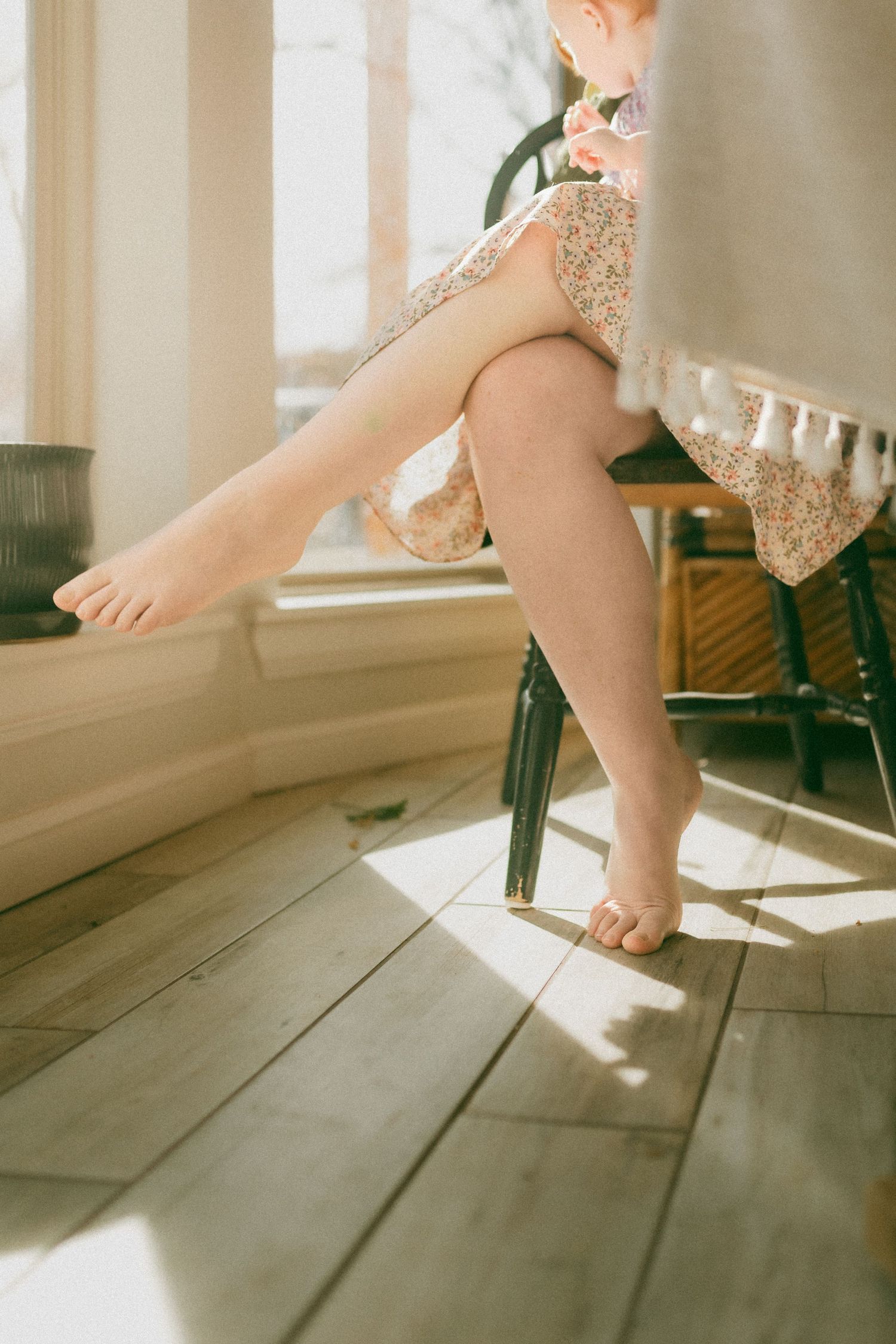 Close-up series of small bare feet walking across sunlit wooden floorboards.