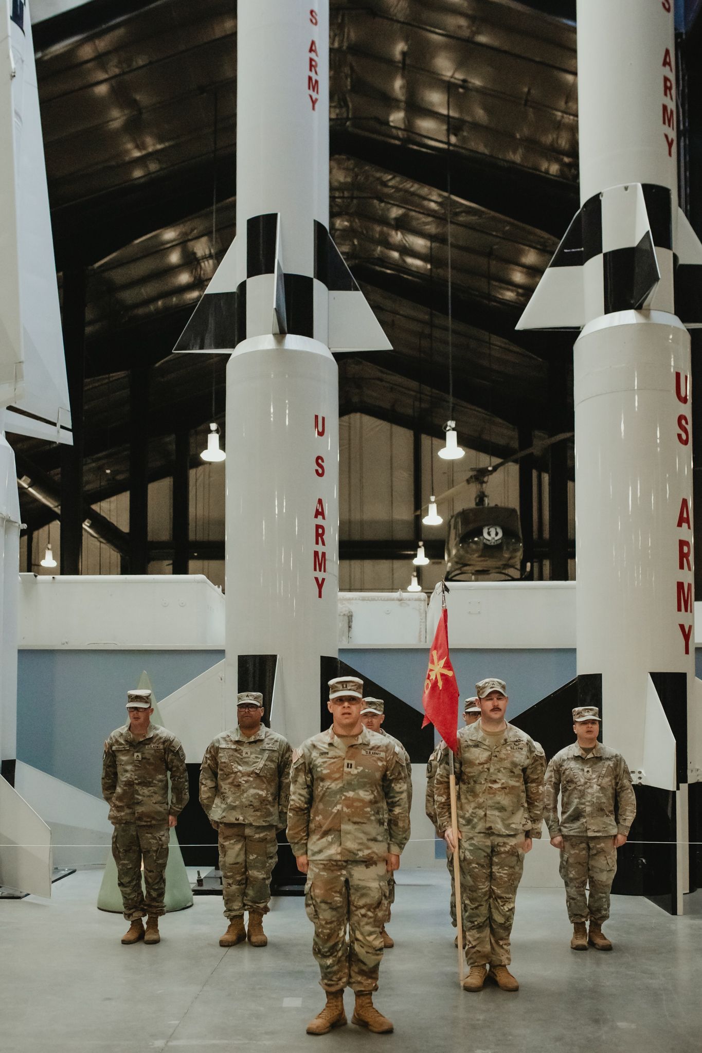 Military personnel stand in formation next to white missile display models in a covered facility.
