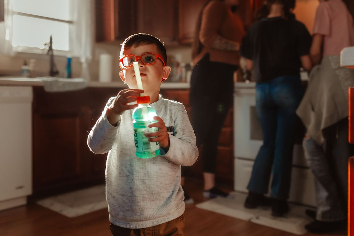 Young child holding a glowing jar in a dimly lit kitchen.