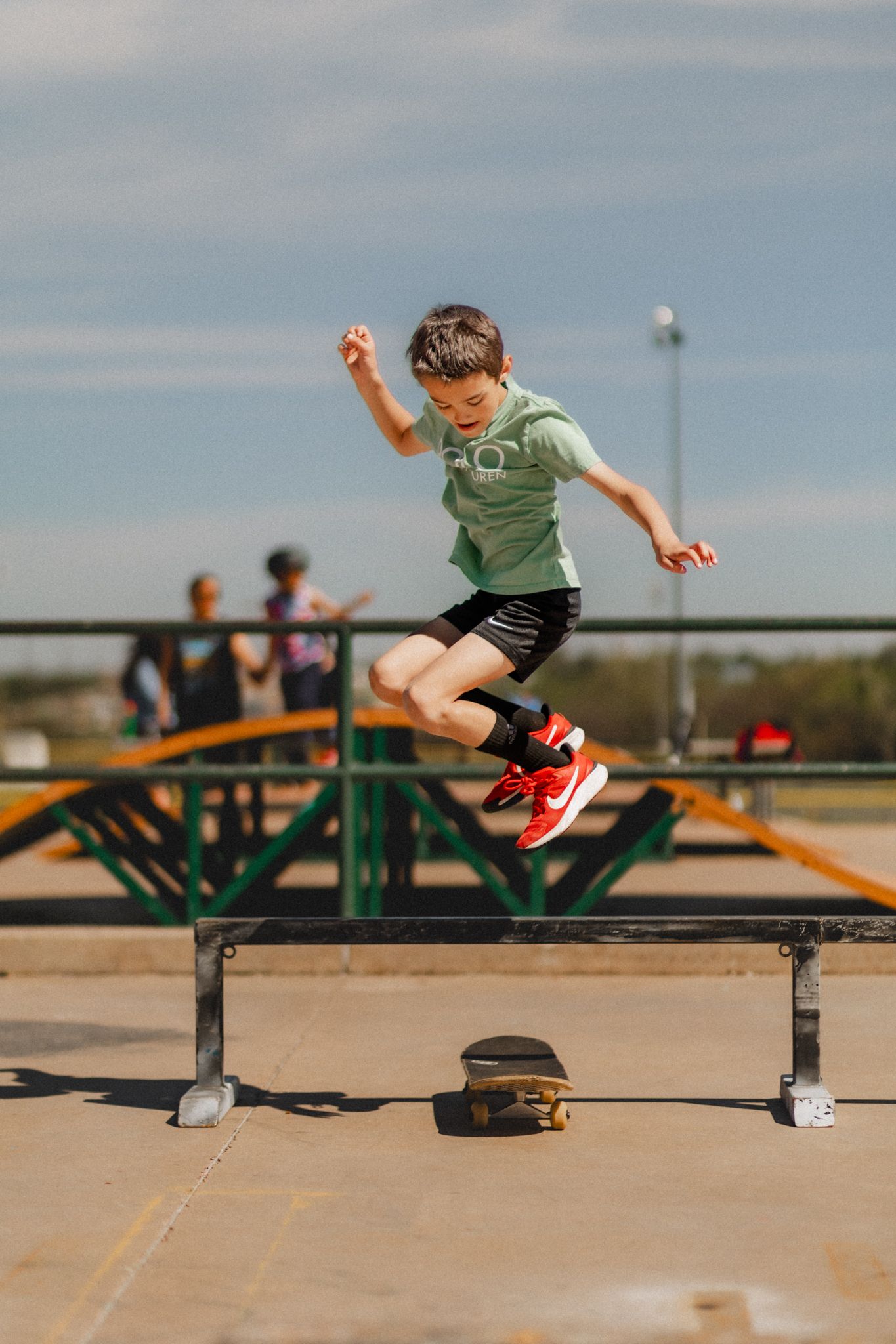 Skateboarder performing a trick jump over a barrier at a skate park on a sunny day.