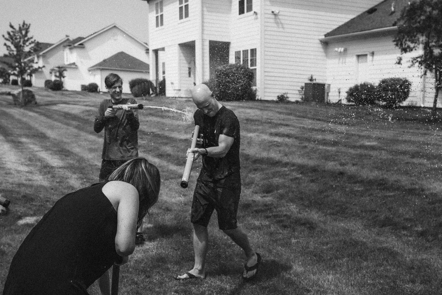 Black and white photo of people playing with water guns in a suburban yard.
